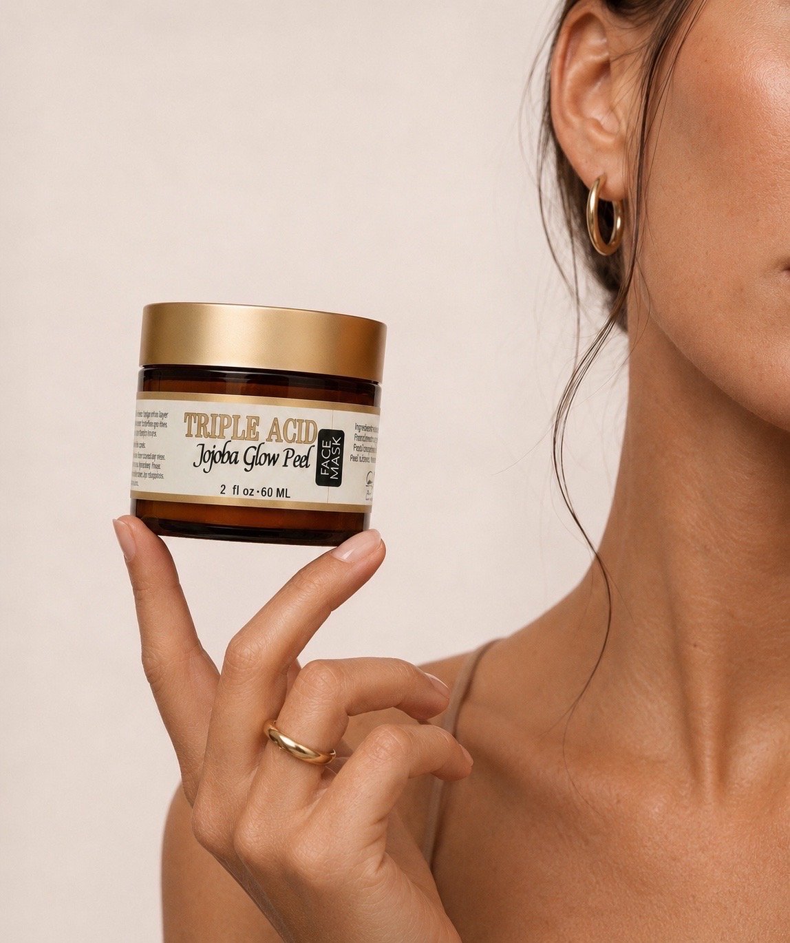 Mature woman holding Innes Ageless Beauty Triple Acid Jojoba Glow Peel face mask in a 2 oz amber jar