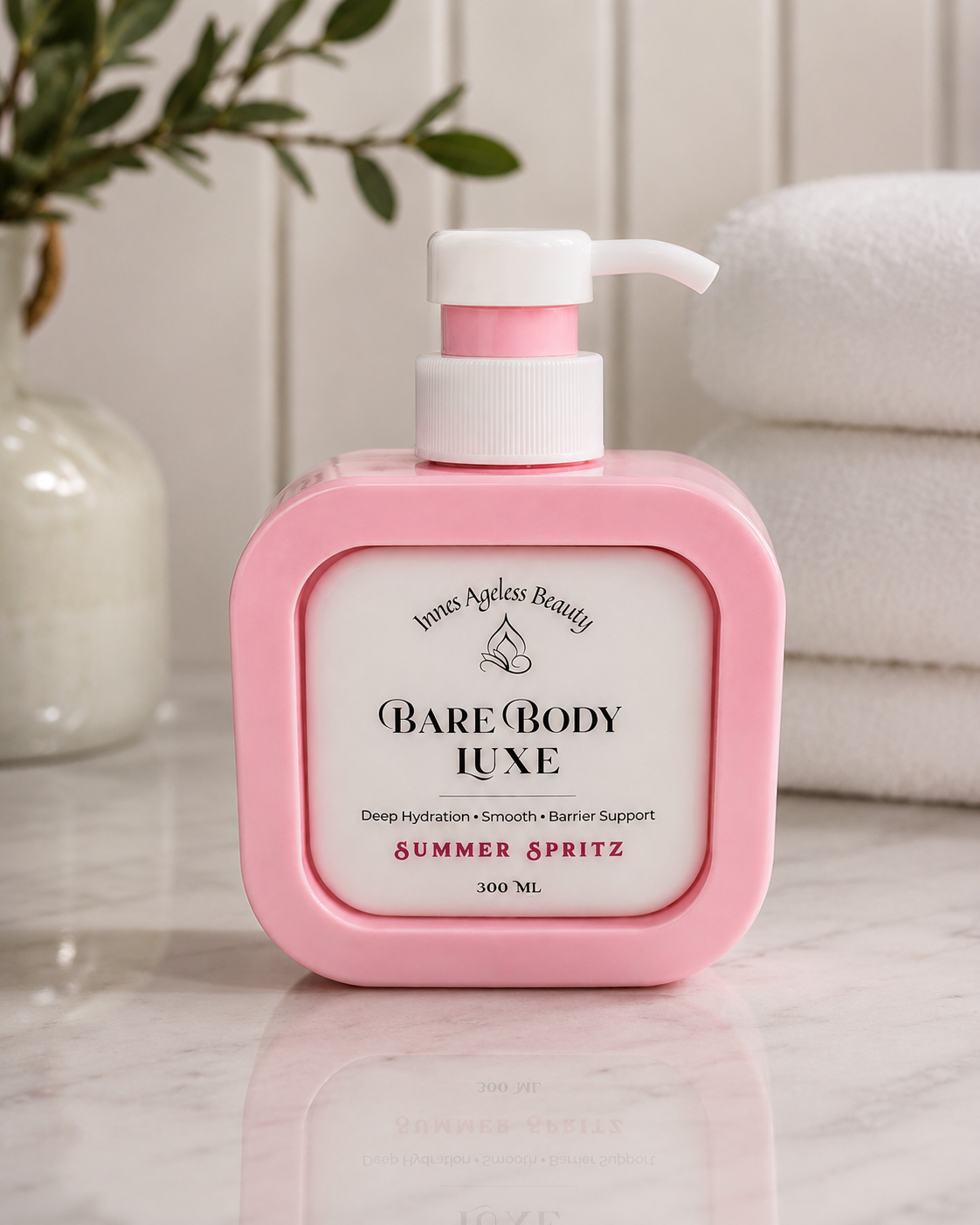 Innes Ageless Beauty Bare Body Luxe Summer Spritz in a pink 300 mL pump bottle displayed on a marble vanity beside folded white towels.
