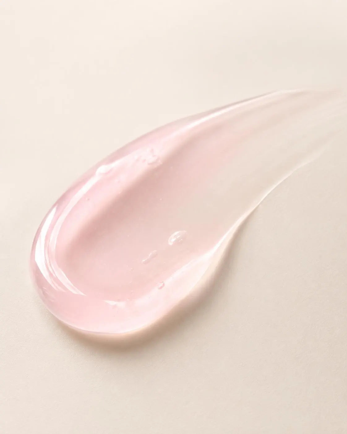 A glossy pink gel smudge with tiny air bubbles on a neutral beige background.