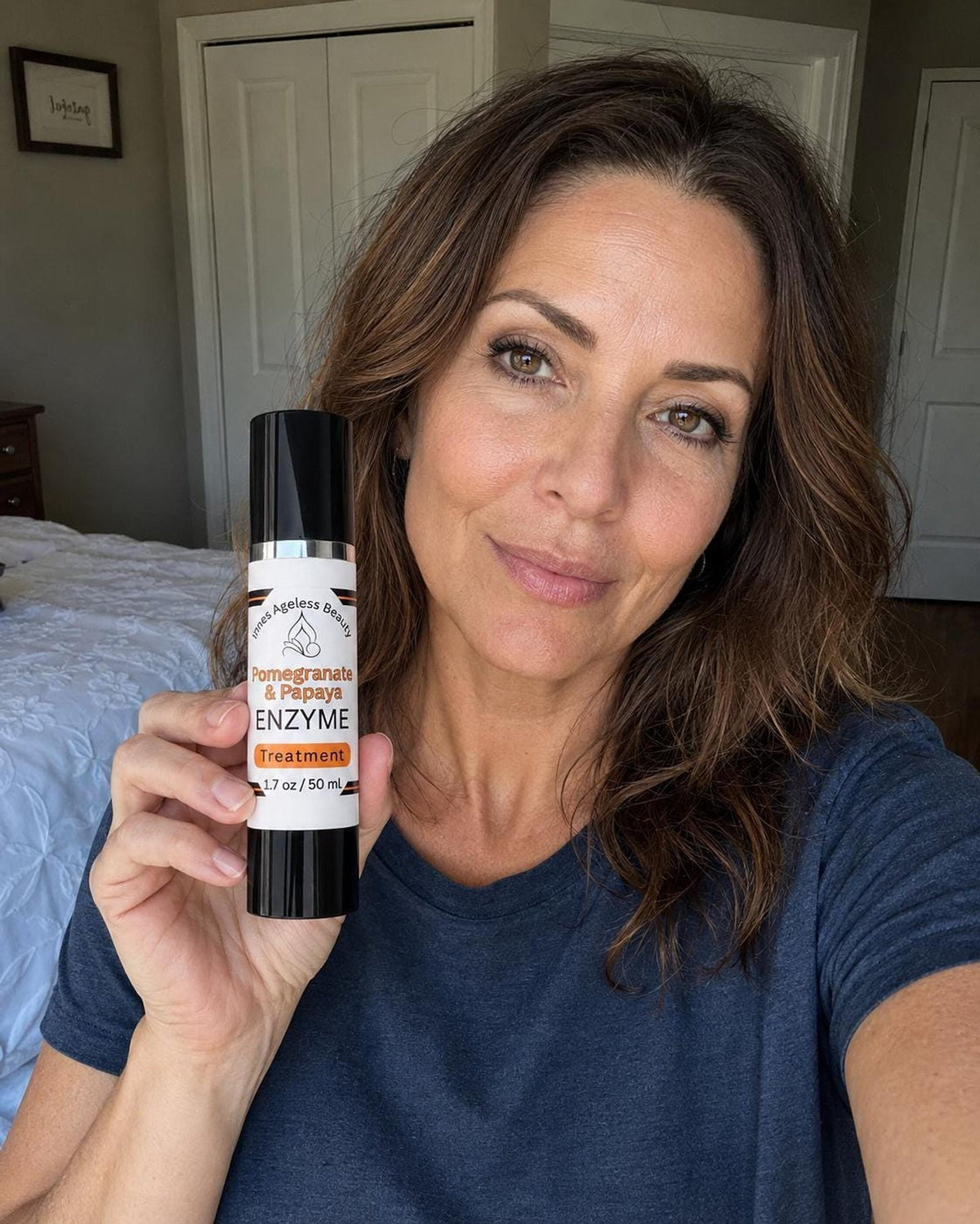 A smiling woman with brown hair holds a white and black pump bottle labeled Pomegranate and Papaya Enzyme Treatment.