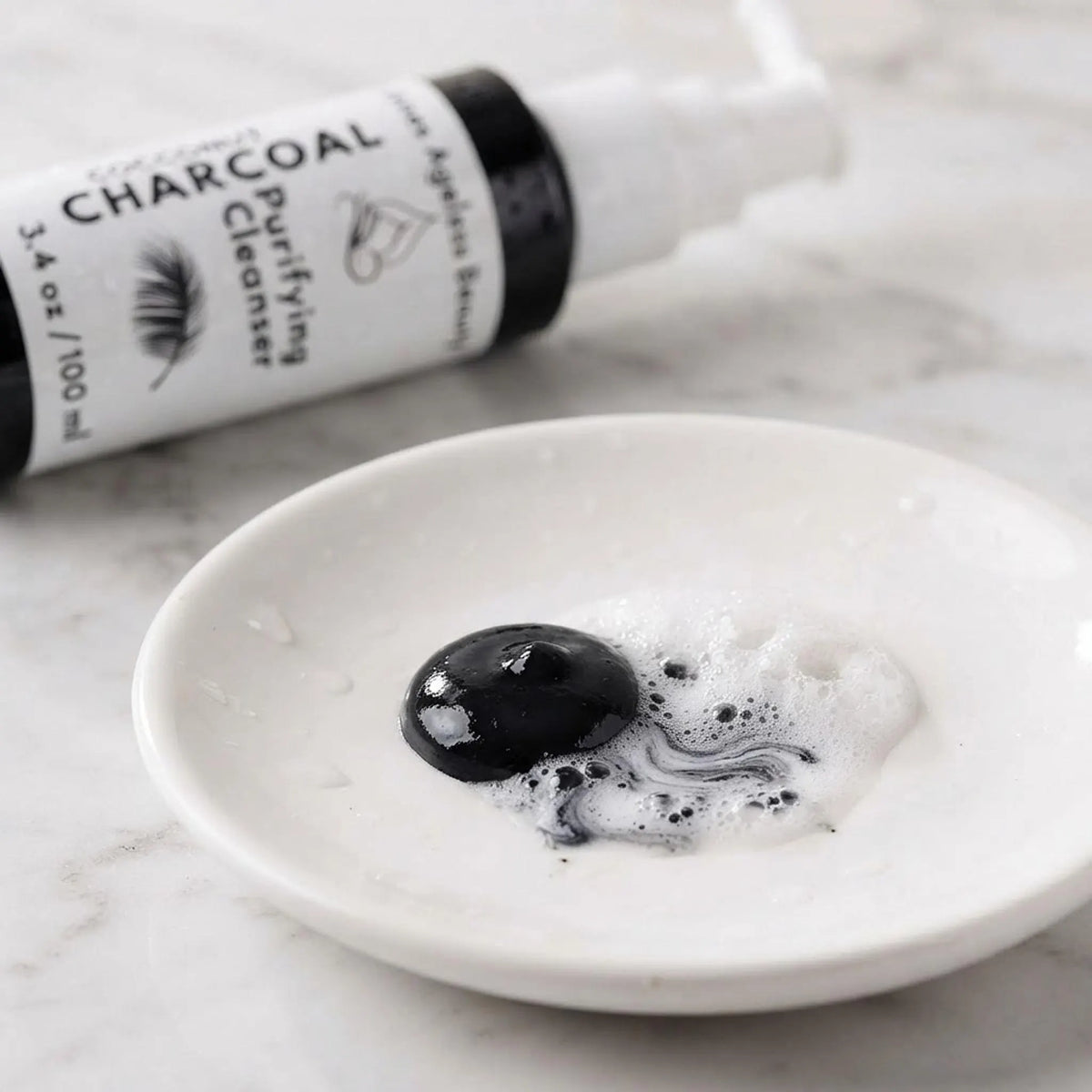 Macro view of black coconut charcoal cleanser gel with silky white lather on a white dish.