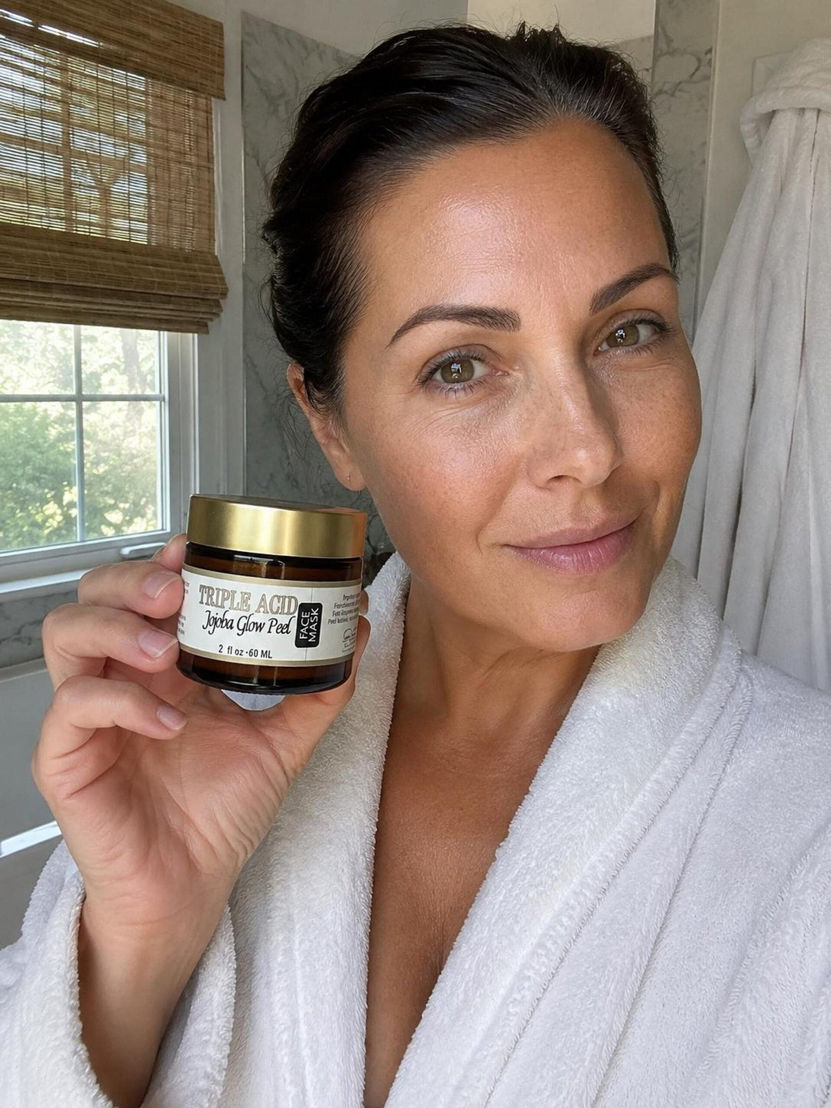 An amber glass jar of Triple Acid Jojoba Glow Peel with its gold lid resting beside it on a surface, showing cream product inside and a dollop in front.