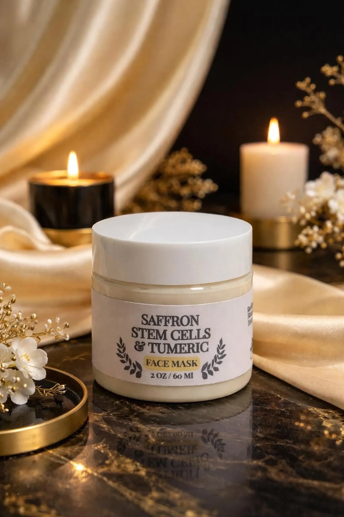A white jar of Saffron Stem Cells & Tumeric face mask is displayed on a dark surface next to lit candles and gold fabric.