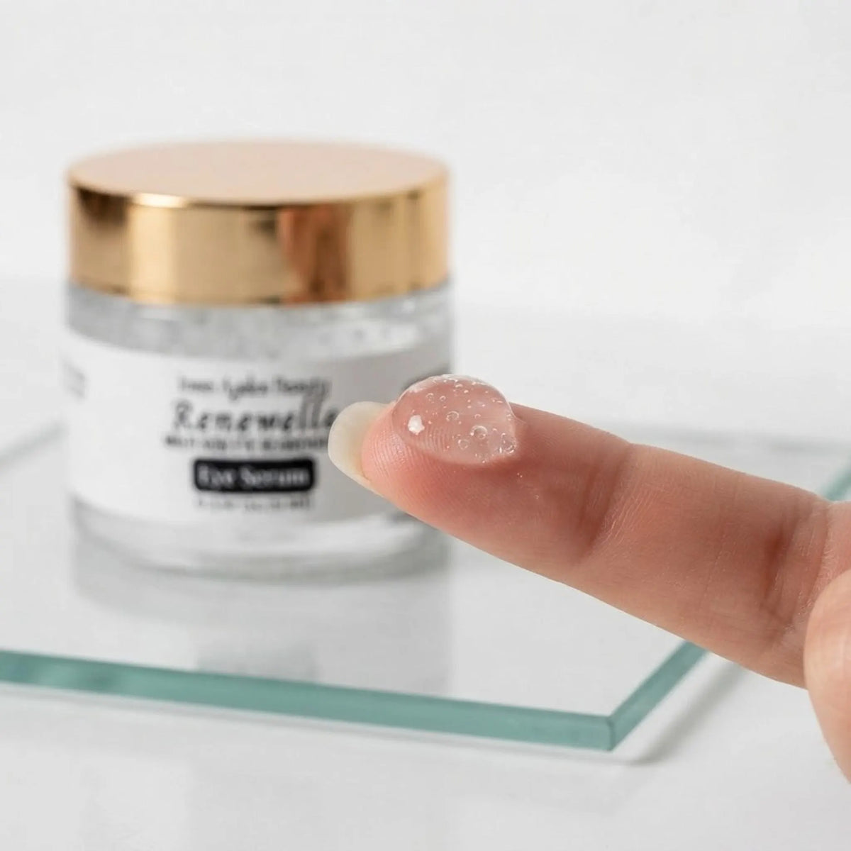 Close-up of the cooling transparent gel texture of the Renewelle eye serum on a fingertip.