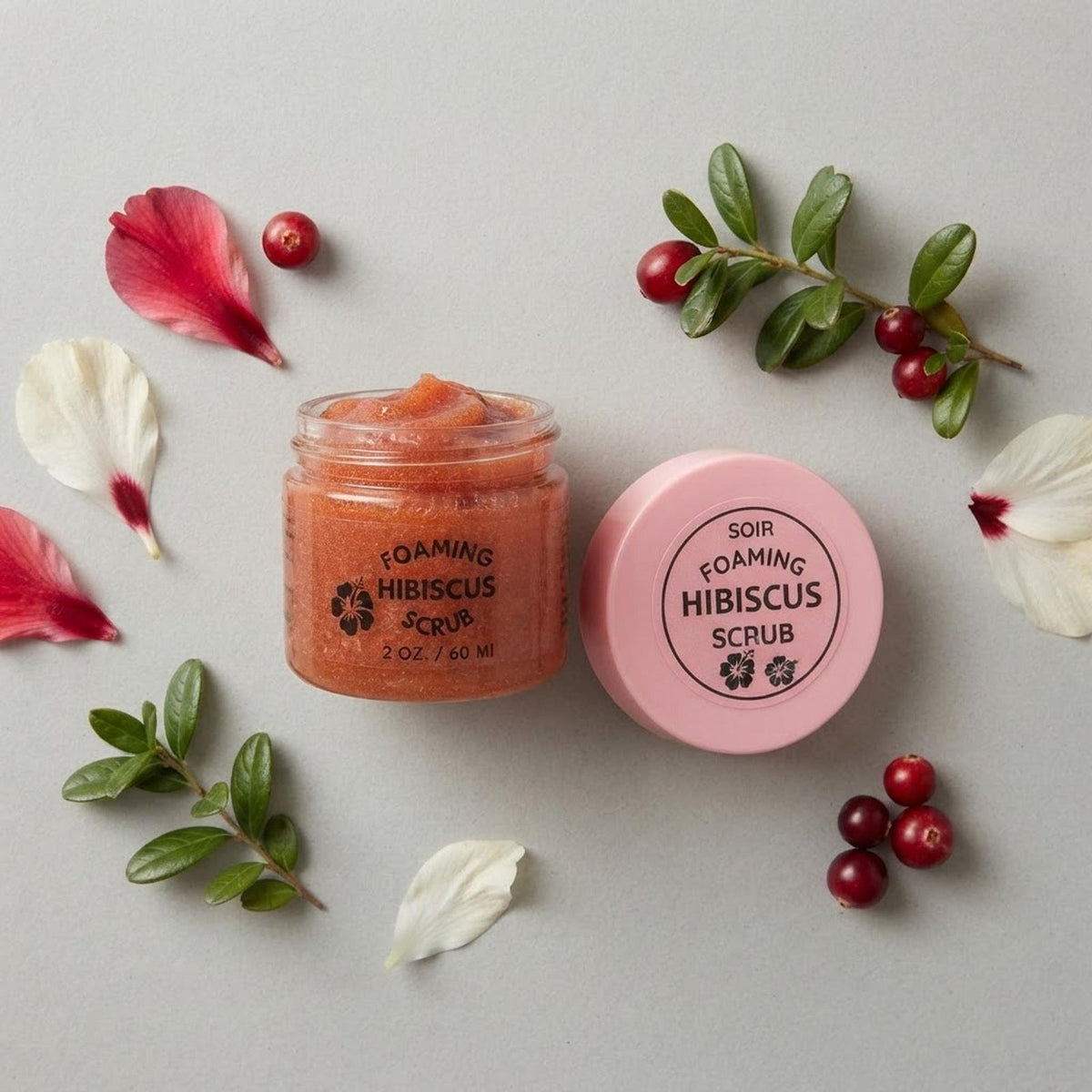 Flat-lay photograph showing the 2 oz foaming hibiscus scrub jar opened with fresh botanical elements surrounding it.