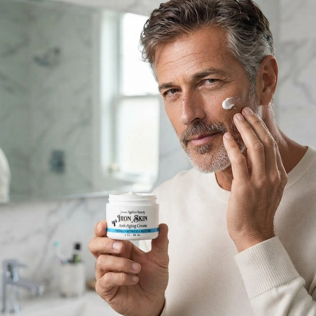 Mature man applying Iron Skin anti-aging face cream to his cheek in a well-lit bathroom setting
