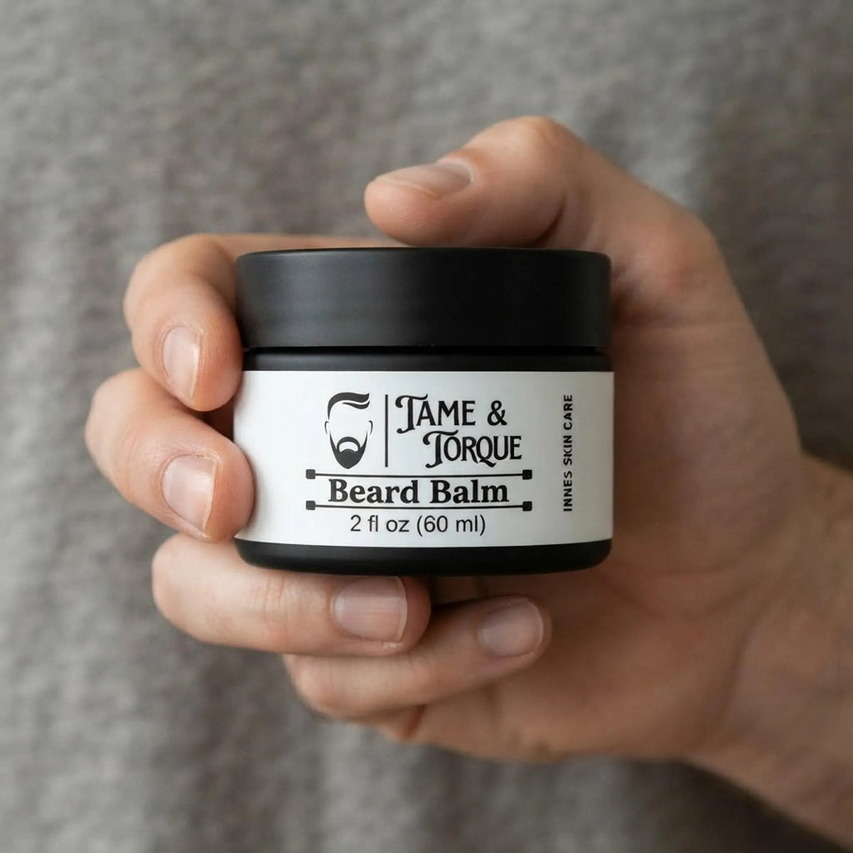Man holding the 2 oz Tame and Torque beard balm jar to show product scale.