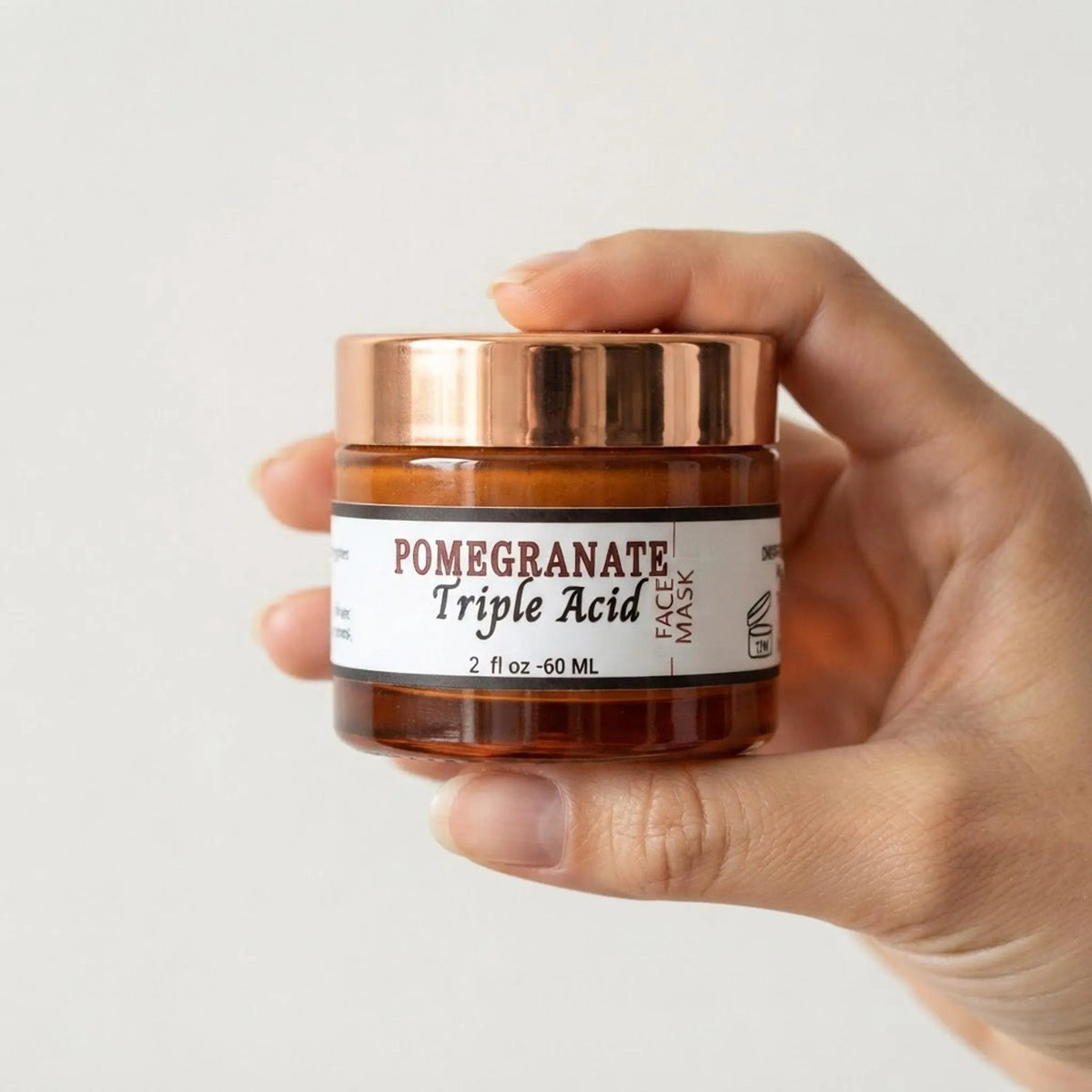 A person holding the 2 oz Pomegranate Triple Acid Face Mask jar to show product scale in hand