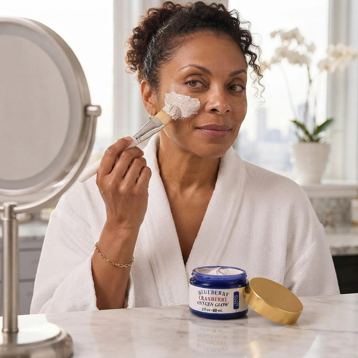A close-up of a person applying the blueberry cranberry oxygen face mask with a brush in a bright bathroom.