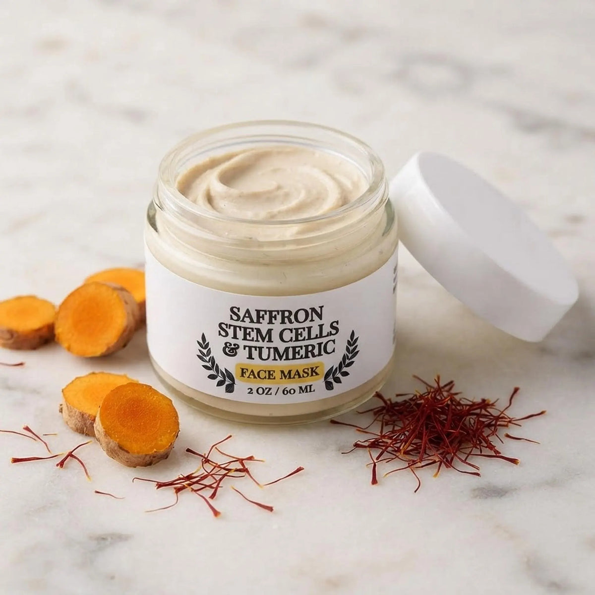 Close up of the face mask jar open, showing creamy texture with fresh turmeric root and saffron threads nearby.