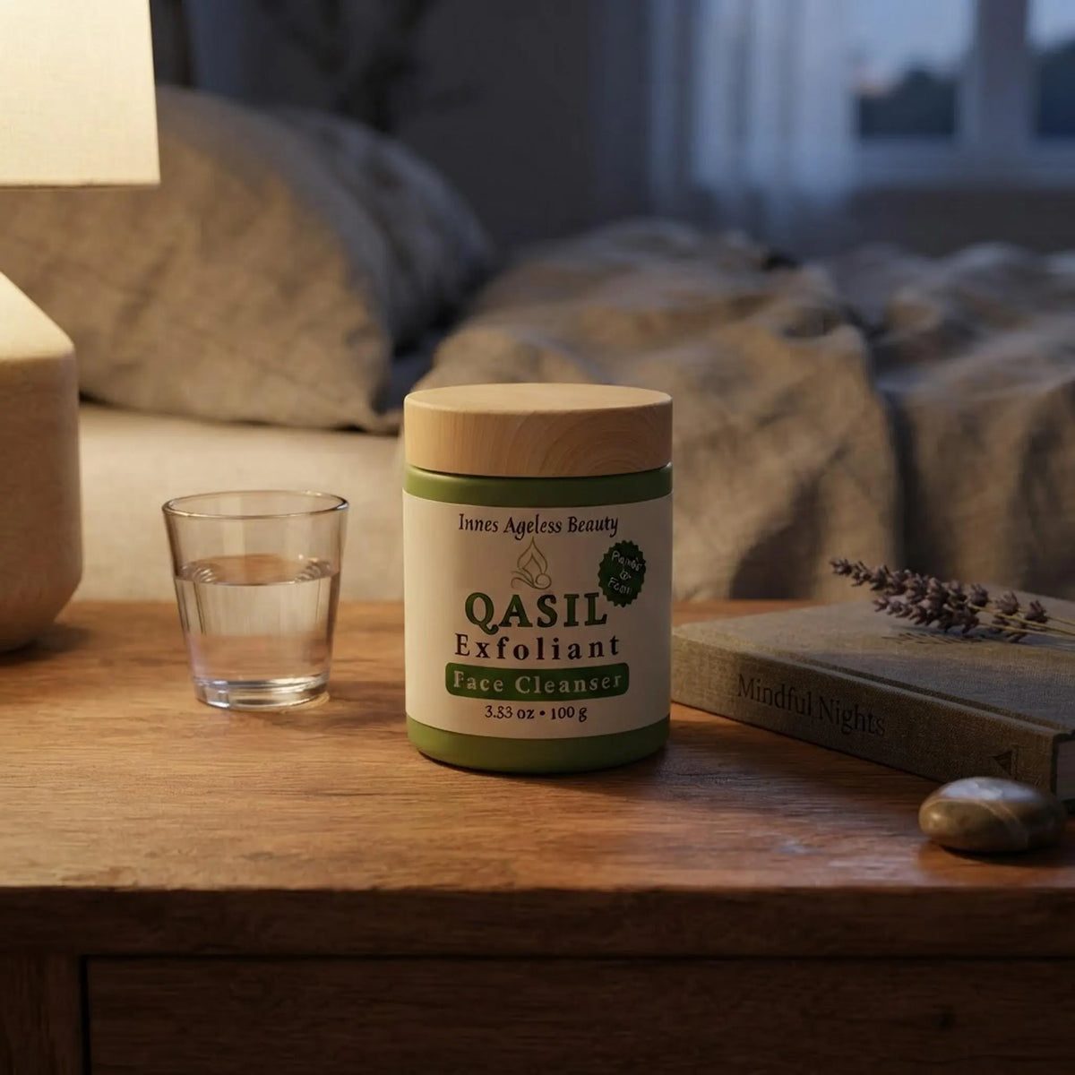 Qasil Exfoliant Face Cleanser jar on a cozy wooden bedside table with warm lighting