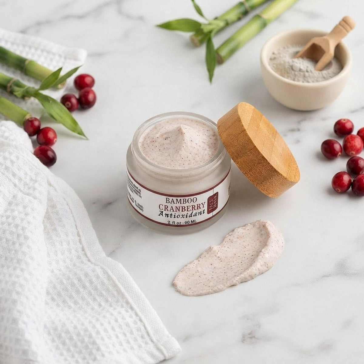 Flatlay of the face mask jar surrounded by bamboo stalks, cranberries, a towel, and ingredients.